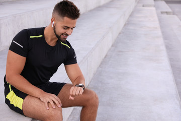 Young man with wireless headphones and smart watch listening to music on stairs