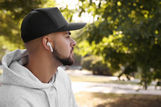 Young man with wireless headphones listening to music in park. Space for text