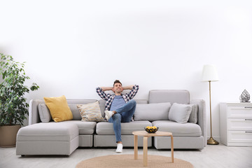 Young man relaxing on sofa under air conditioner at home