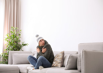 Young man wearing warm clothes freezing on sofa at home. Air conditioner malfunction