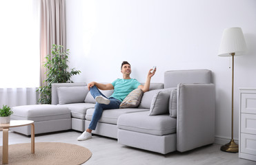 Young man with air conditioner remote control relaxing on sofa at home