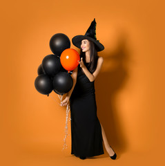 Beautiful woman wearing witch costume with balloons for Halloween party on yellow background