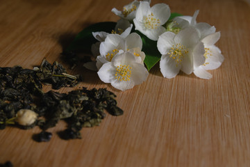 Dry green tea and fresh white jasmine flowers are scattered on a wooden table. Chinese green tea with jasmine. Antioxidant drink.