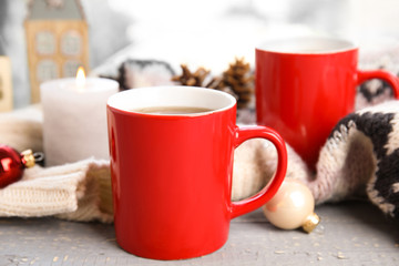 Cups of hot winter drink with scarf on window sill indoors