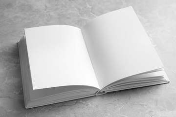 Open book with blank pages on light grey marble background. Mock up for design