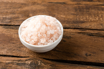 Pink Himalayan salt in bowl on vintage wooden background. Close up