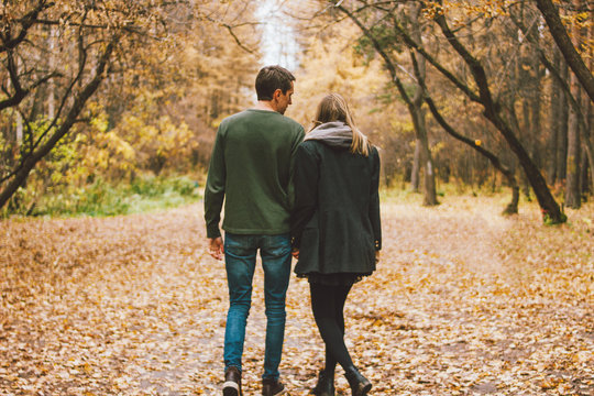 Young couple in love friends dressed in casual style walking together on autumn park, people from behind