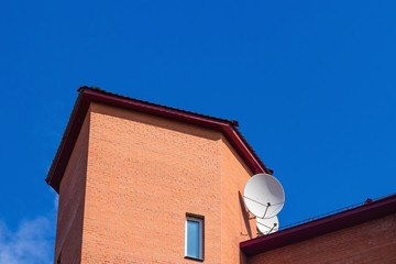 Satellite dish on the roof of a brick house on a background of blue sky