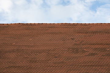 Old red metal tile roof against sky