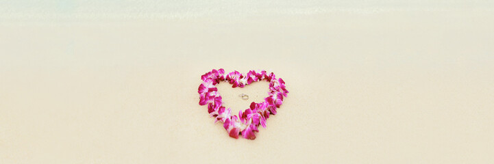 Beach wedding proposal rings in heart shap lei flowers necklace on white sand Hawaii honeymoon. Two...
