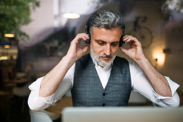 Mature man with headphones at the table in a cafe, using laptop.