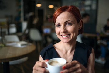 Portrait of woman sitting in a cafe, holding a cup of coffee.