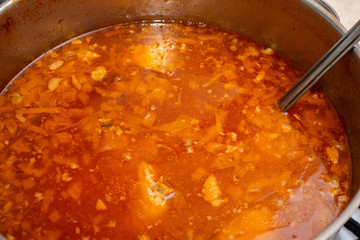 Red borsch with cabbage and fat rich meat in a pan, close-up from above.