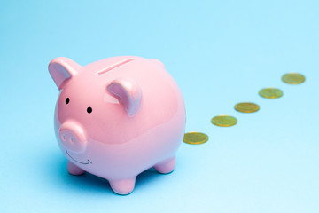 Loss of money. Pink piggy bank losing gold coins on blue background. Bad investment or falling profits
