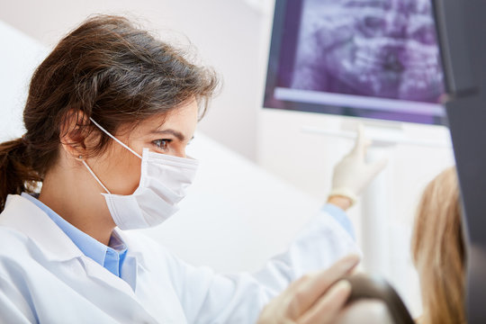 Zahnärztin mit Mundschutz zeigt auf Röntgenbild