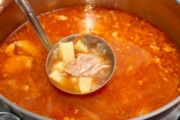Red borsch in a saucepan with cabbage and fat, meat in a soup ladle.