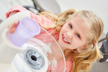Kind beim Zahnarzt mit einem Plastikbecher Wasser