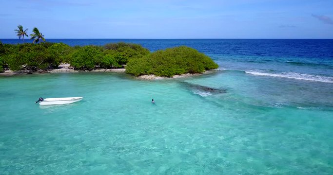 extreme wide shot of a lovely tiny island in the  Caribbean, a single man swimming near his abandoned boat.
