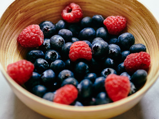 Blueberries and Raspberries detail in a wooden bowl on a white marble
