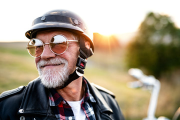 A cheerful senior man traveller with motorbike in countryside, headshot. - obrazy, fototapety, plakaty