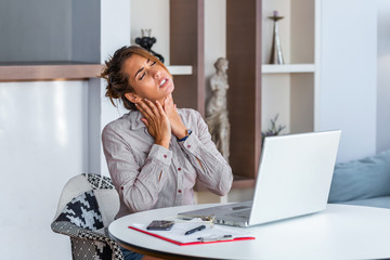 Businesswoman feeling pain in neck after sitting at the table with laptop. Tired female suffering of office syndrome because of long hours computer work. Pretty girl massaging her tense neck muscles