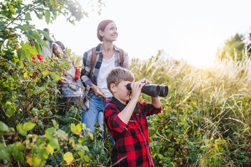 Fototapeta premium Group of school children with teacher on field trip in nature, using binoculars.