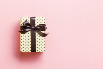 Gift box with black bow for Christmas or New Year day on pink background, top view with copy space