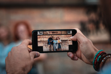 Group of tourists enjoying on vacation, young man photographing his friends with smart phone.