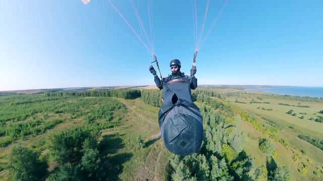A person is flying the paraplane over the forest in a front view