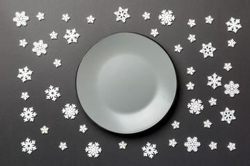 Top view of empty plate surrounded with snowflakes on colorful background. New Year dinner concept
