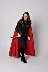 full length portrait of a pretty brunette woman wearing black leather fantasy costume with long red...
