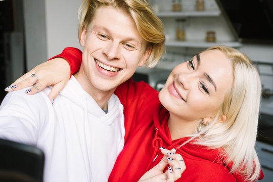 Smiling happy blonde couple using cell phone. Selfie time! Adorable smilimg friends. Standing at the kitchen