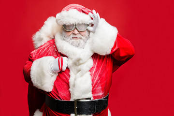 Portrait of smart confident elderly strict santa claus fix his goggles ready to carry his big sack bag with present gifts wear white gloves costume belt cap isolated over red color background