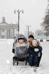 Fototapeta na wymiar Young happy mother and her two adorable little kids having fun on winter day at city