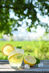 Glasses of lemon juice on a wooden table, summer set, outdoor greed blured background,boke.Water detox