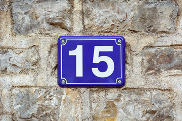 Blue house number fifteen on a stone wall background