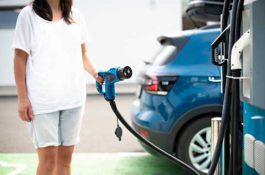 Woman charge Electric car on gas station. Blue car and electric plug for charging.