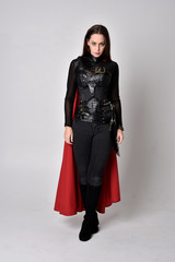 full length portrait of a pretty brunette woman wearing black leather fantasy costume with long red...