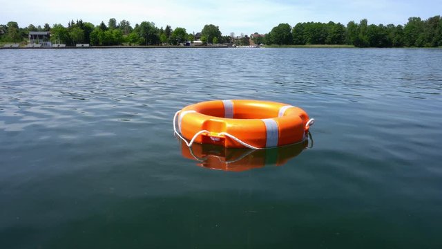 Orange lifebuoy floating on lake water far away from shore. Gimbal motion