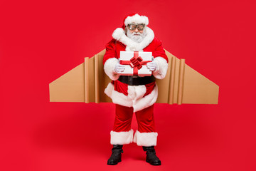 Full length photo of cool funky aviator santa claus in cap hat give craft package to kids in christmas night wear belt boots pants isolated over red background