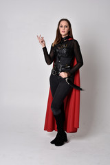 full length portrait of a pretty brunette woman wearing black leather fantasy costume with long red...