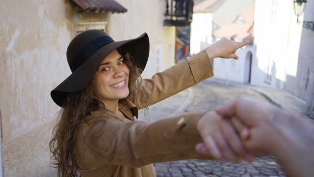 Young Lady and man walking at downtown of Prague. Close-up portrait joyful girl leading boyfriend down on narrow street between residential houses, smiling and enjoying togetherness. Follow me concept