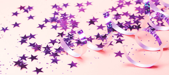 Shiny party streamers and stars on the pink background. Banner format. Close up. The concept of celebrations, the Day of St. Valentine, Christmas, New Year, holiday, birthday, etc.