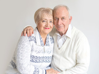 Happy senior citizens in white clothes sitting hugging on a white background