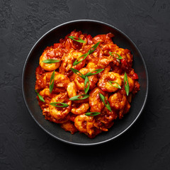 Schezwan Prawns in black bowl at dark slate background. Schezwan Prawns is indo-chinese cuisine curry dish with prawns or shrimps roasted in Schezwan Sauce.