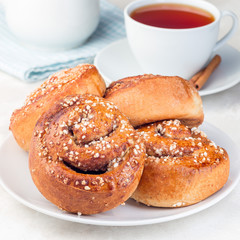 Cinnamon buns on  white plate, served with a cup of red tea, square format