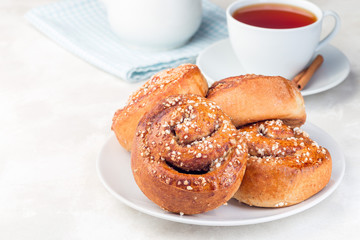 Cinnamon buns on a white plate, served with a cup of red tea, horizontal, copy space