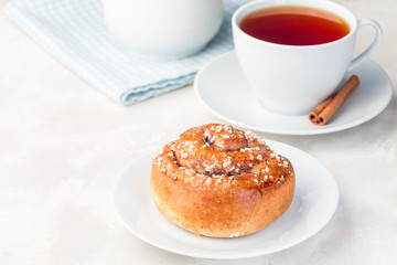 One cinnamon bun on a white plate, served with a cup of red tea, horizontal, copy space