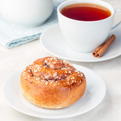 One cinnamon bun on a white plate, served with a cup of red tea, square format, closeup
