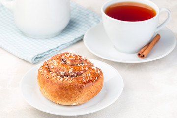 One cinnamon bun on  white plate, served with a cup of red tea, horizontal